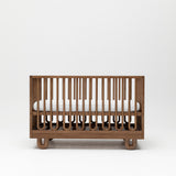 Curved design baby cot with mattress and adjustible base showing mattress at highest height