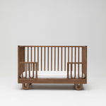 Solid wood Sacred Bundle Arche cot in walnut showing the toddler conversion kit lowered