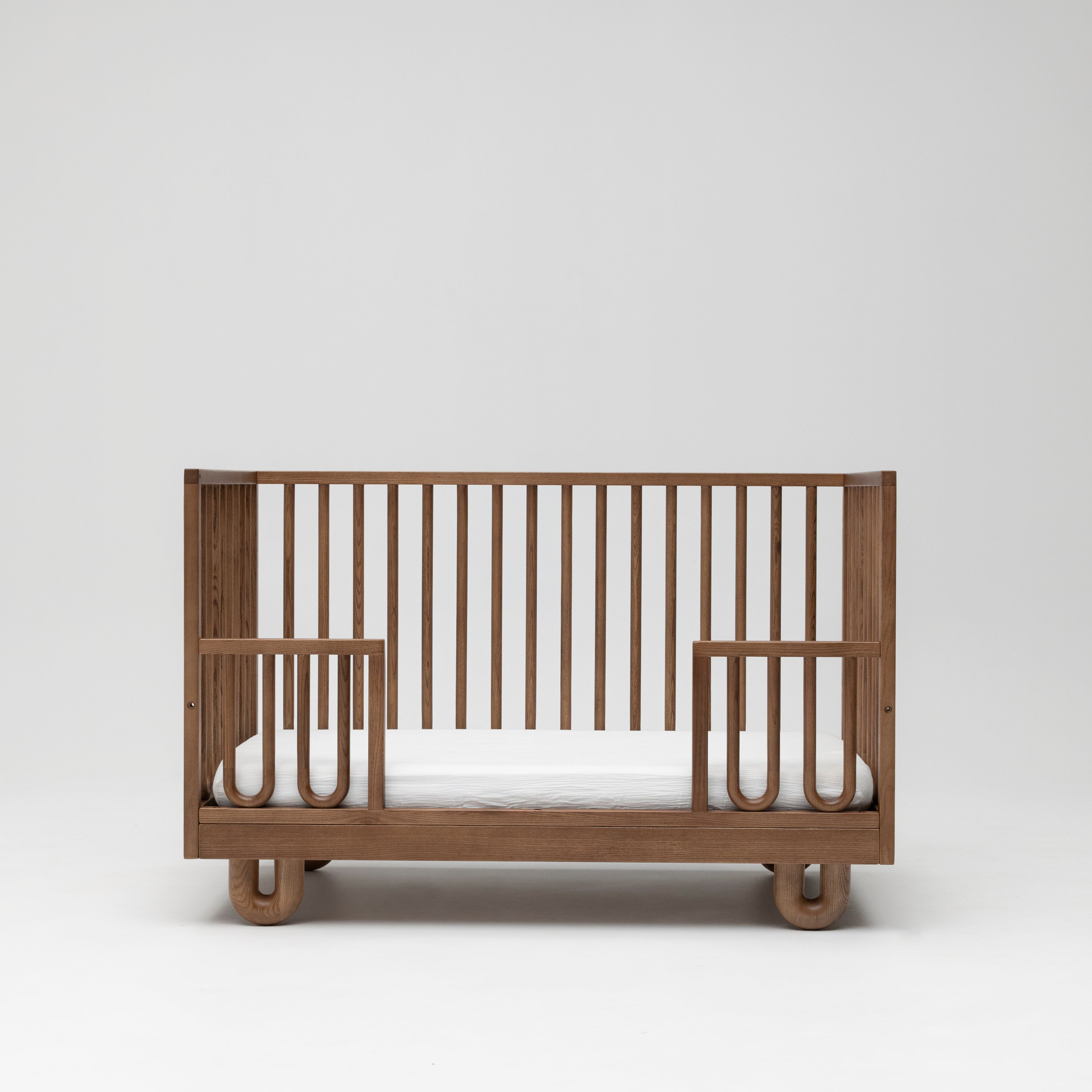 Solid wood Sacred Bundle Arche cot in walnut showing the toddler conversion kit lowered