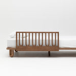 The Arche Walnut Toddler Bed Side Rail attached to the side of an Arche King Single Bed in Walnut with a white mattress