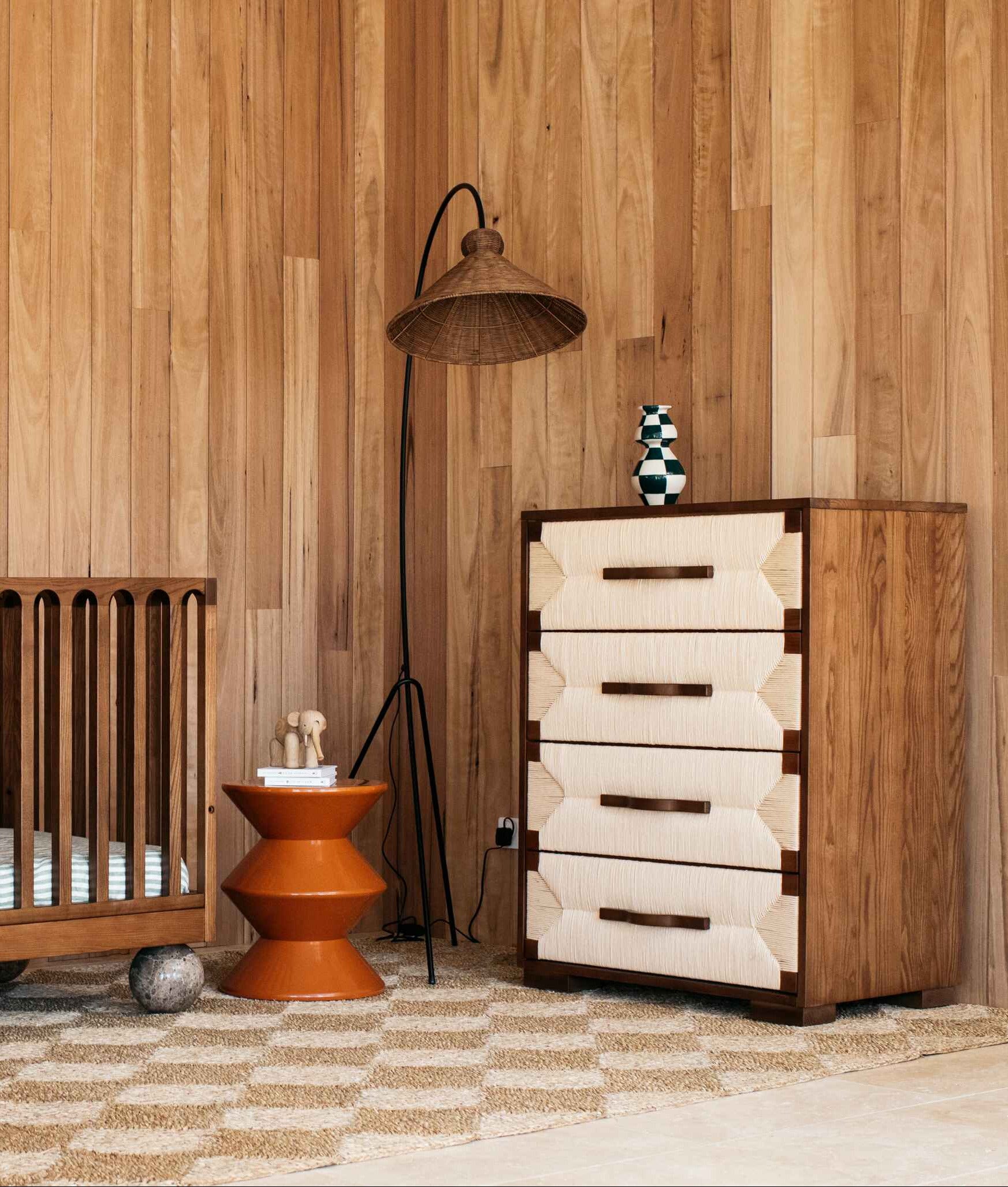 Nursery with solid wood cot, tallboy buffet, and wall art in a room with wooden walls.