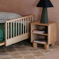Styled image of the Hendrix Ashwood Toddler Bed Side Rail on a single bed with the Hendrix Bed Side Table and a lamp in a kids room