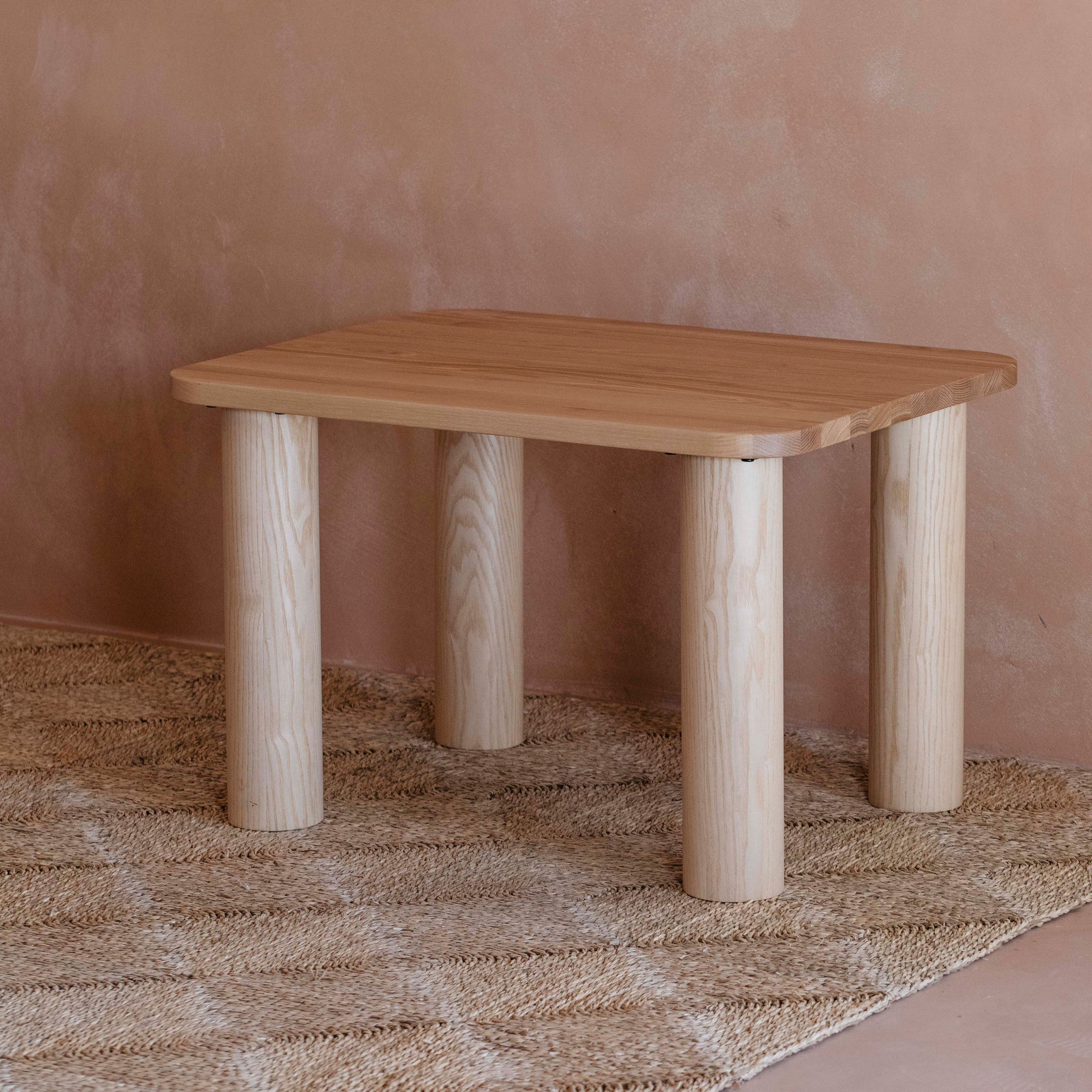 Side view of the Kids Ashwood Hennie Table in a warm toned children's room on a natural woven rug