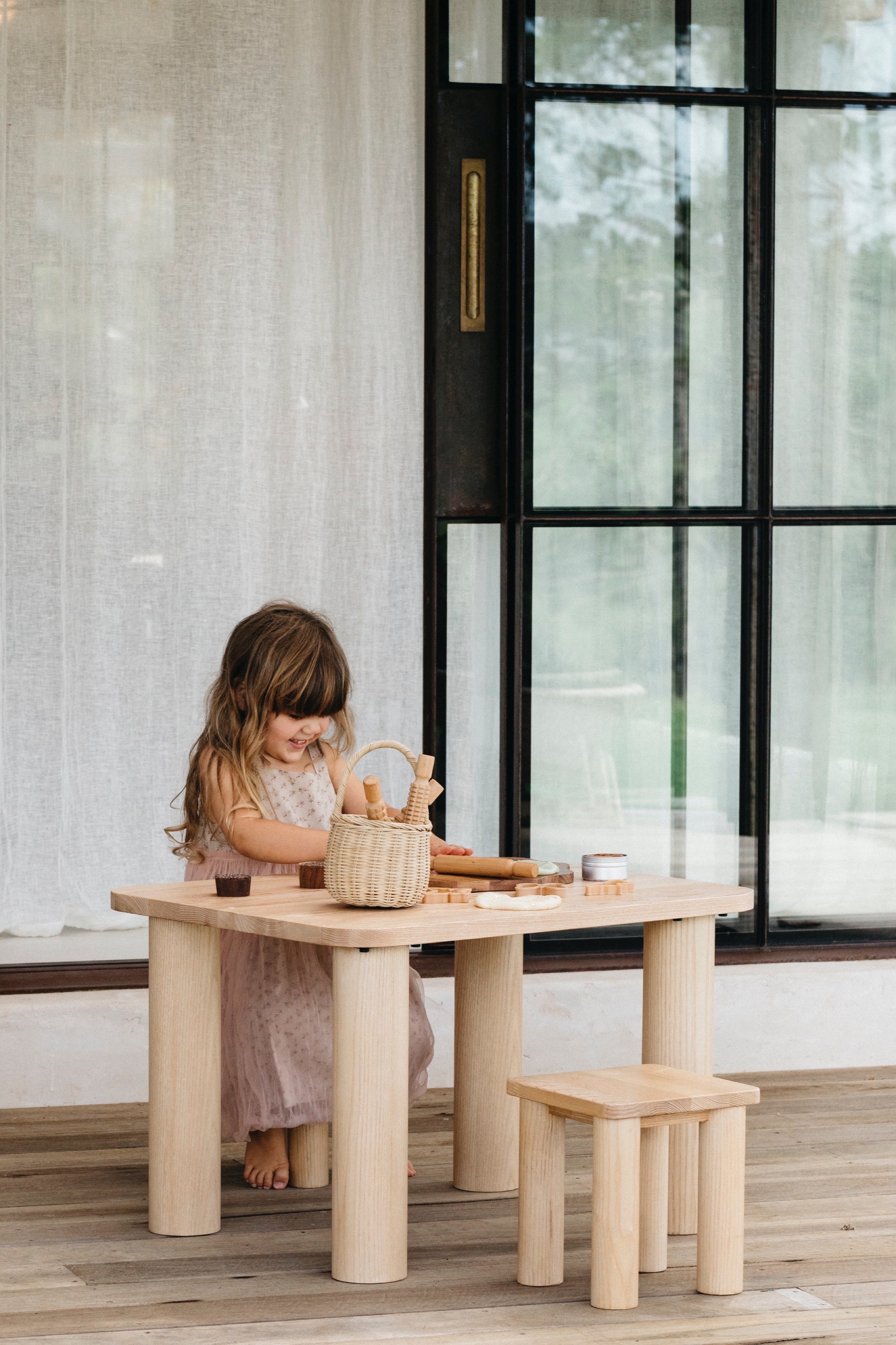Little girl playing with toys outside sitting at a Hennie table on a Hennie Kids Stool, both in Ashwood