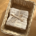 Beige baby wash cloth with a bow in a woven basket on a wooden surface