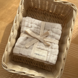 Beige baby wash cloth with a bow in a woven basket on a wooden surface