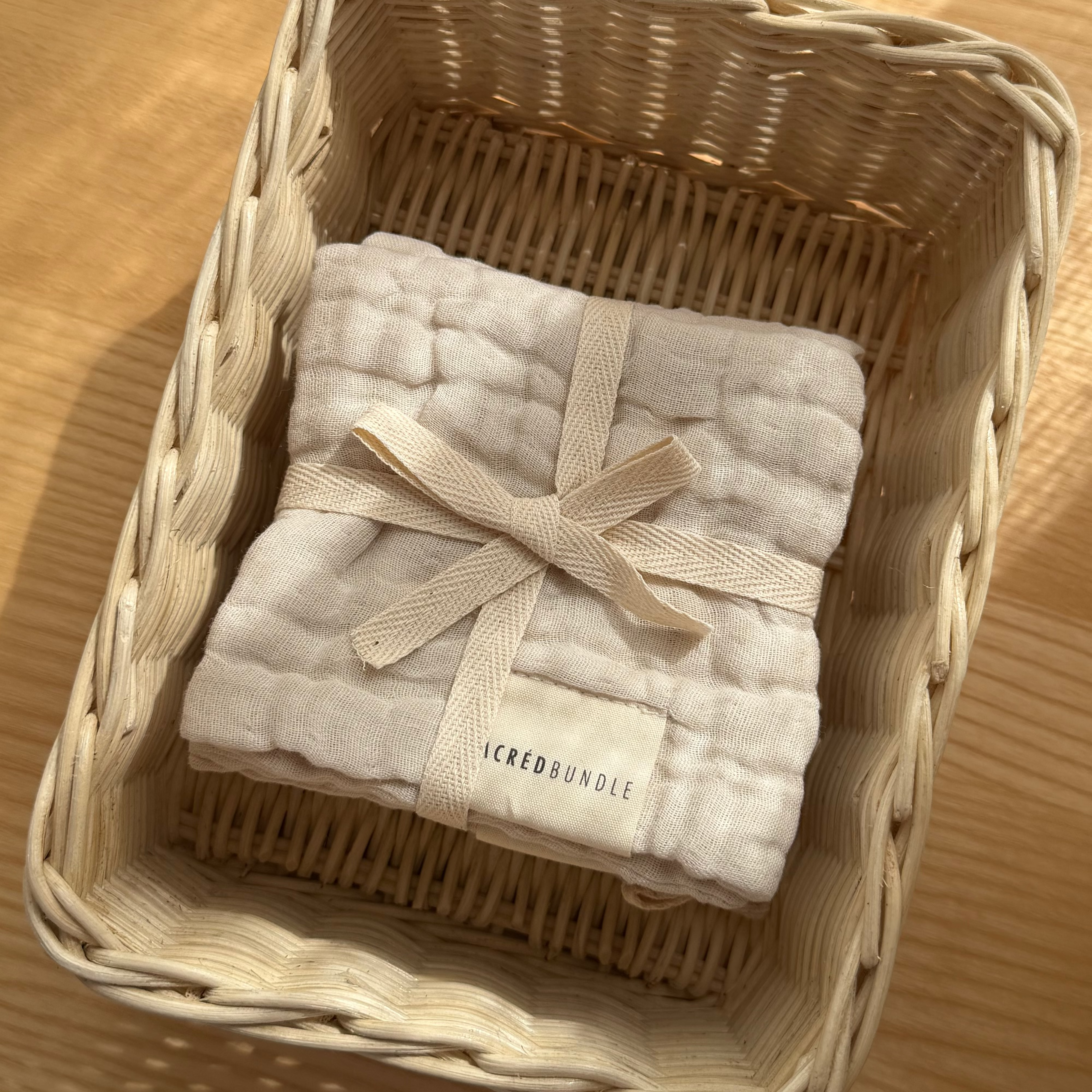 Beige baby wash cloth with a bow in a woven basket on a wooden surface