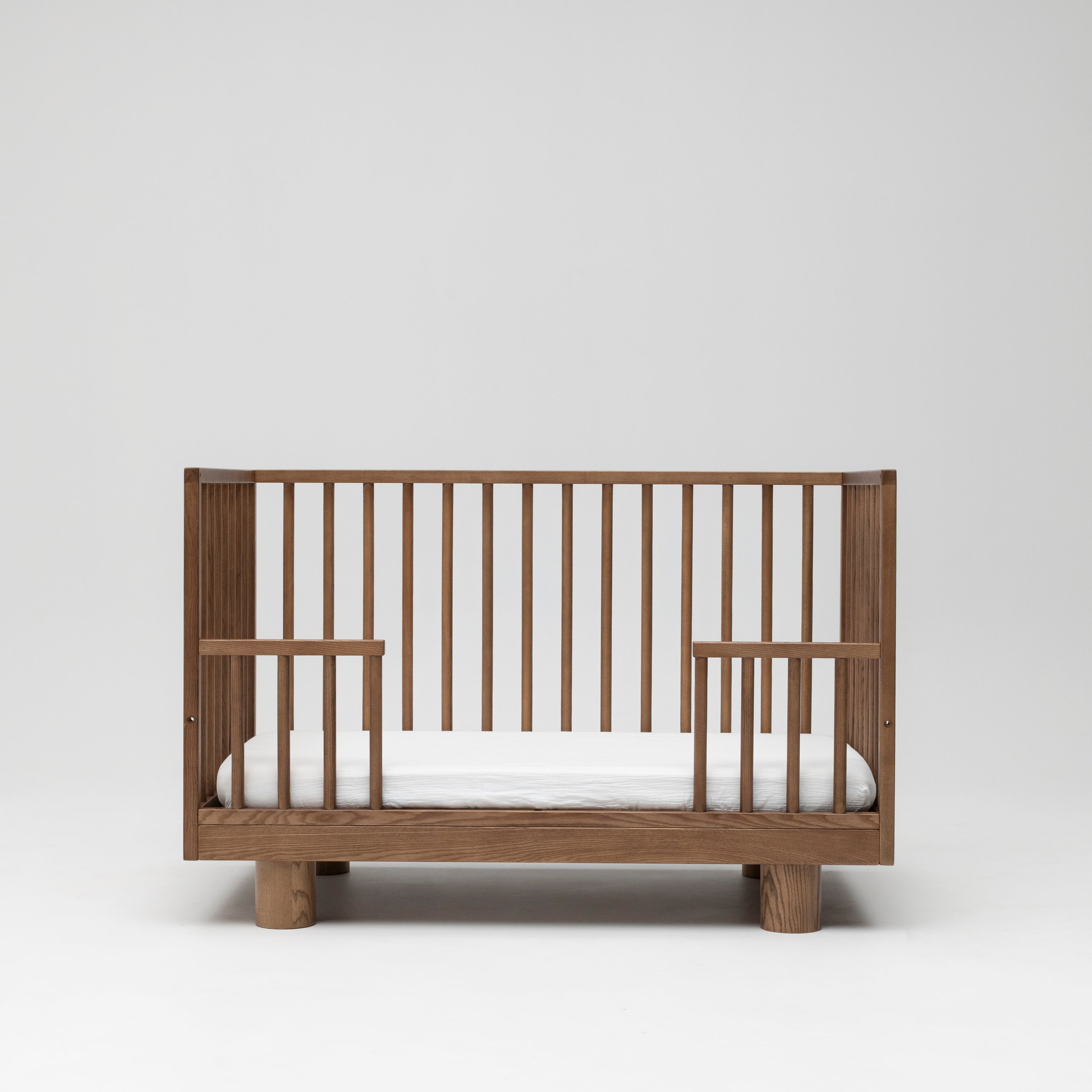 Solid timber baby cot in walnut showing toddler conversion side lowered