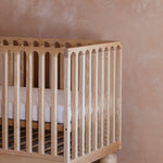 Side view of natural solid timber cot showing round ball legs and curved frame