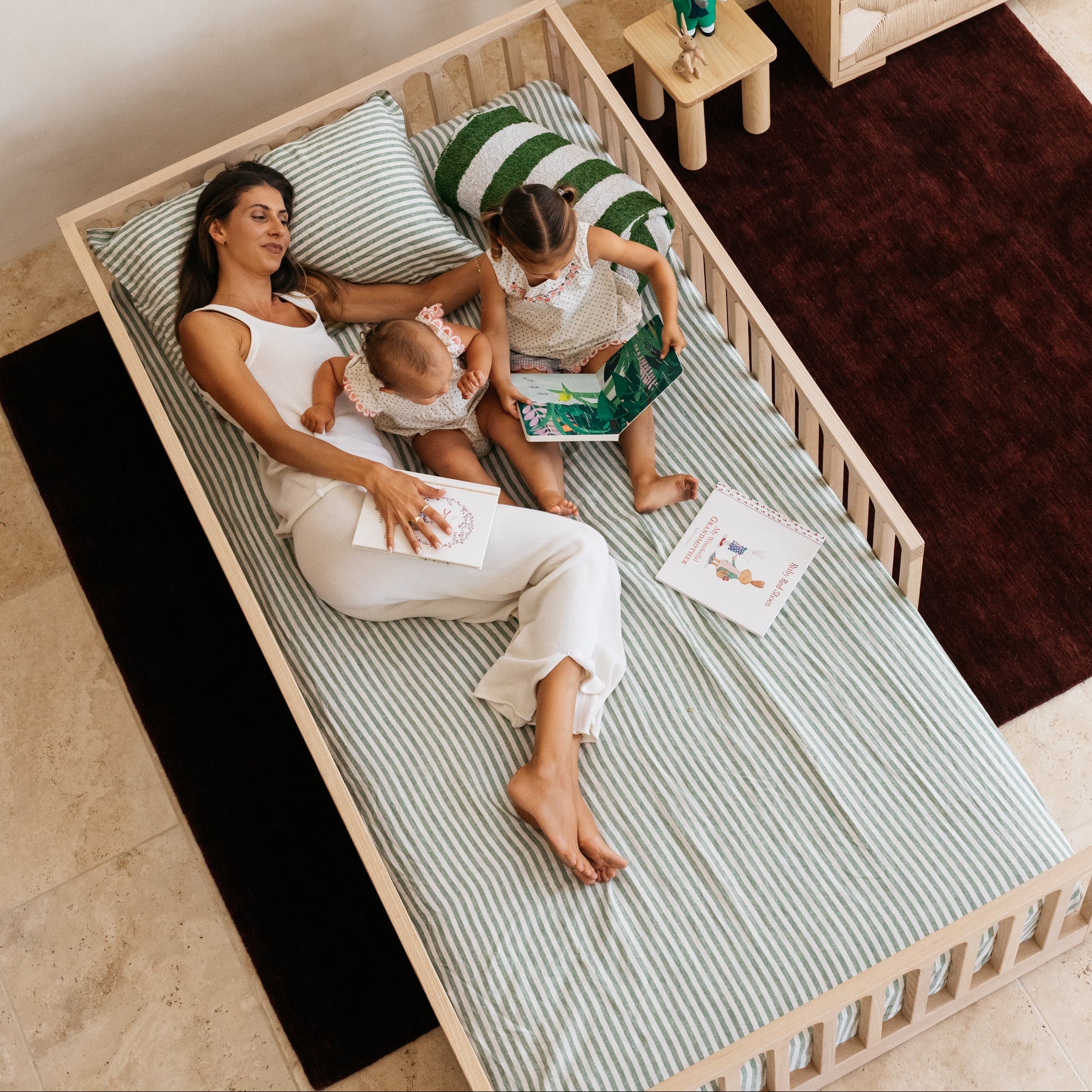 Lifestyle image shot from above showing a Mum, child and baby reading books in the Zali Ashwood Floor Bed in a kids nursery room