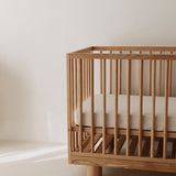 Side view of Ashwood cot showing Hendrix design featuring cylinder legs and solid wood frame with adjustable base