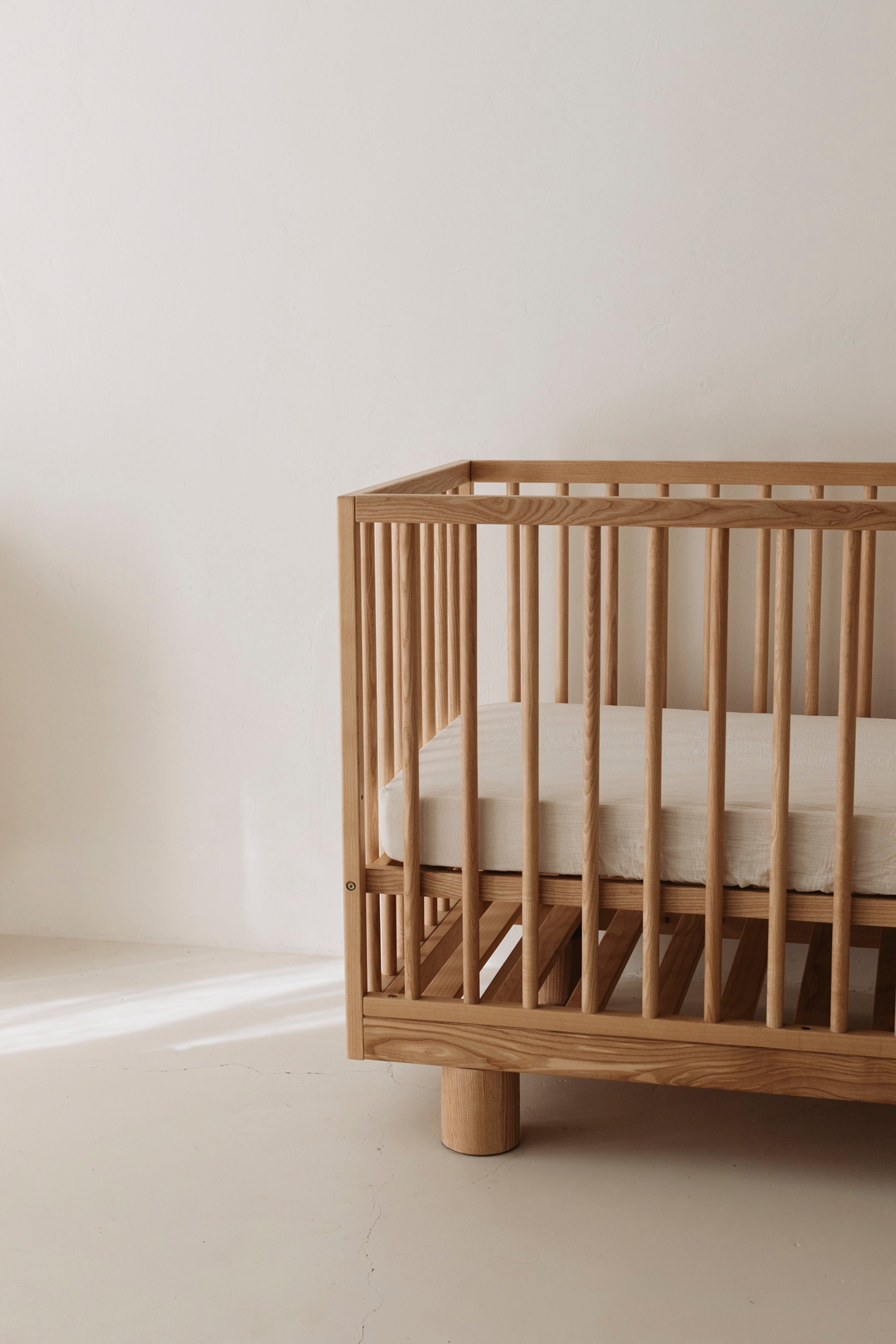 Side view of Ashwood cot showing Hendrix design featuring cylinder legs and solid wood frame with adjustable base